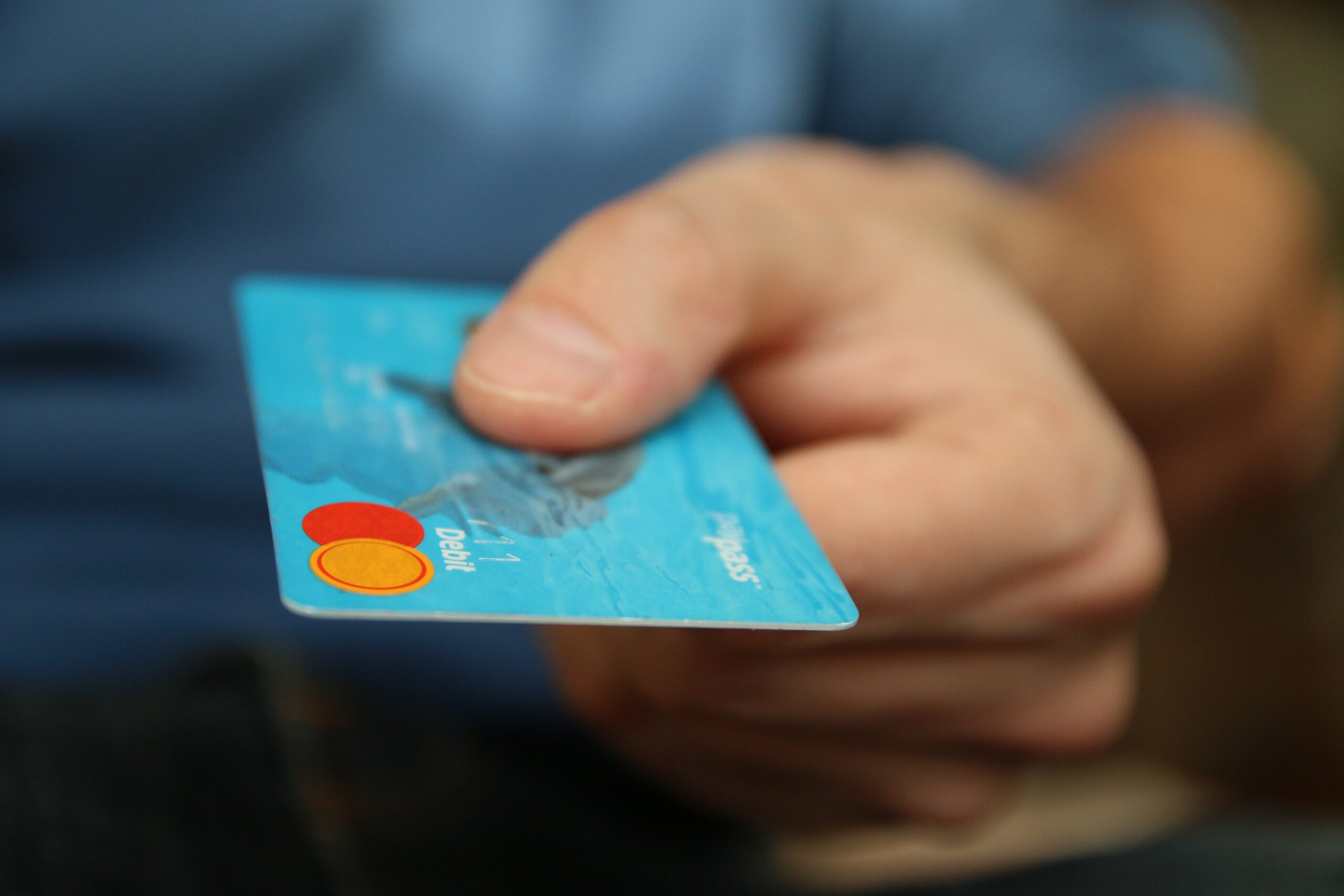 Dłoń trzymająca niebieską kartę do bankomatu