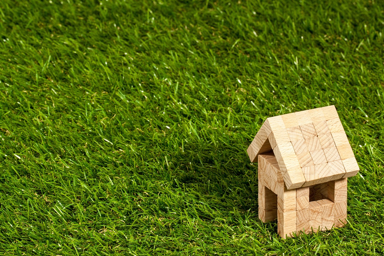 Figurka małego drewnianego domu, stojącego na zielonej trawie